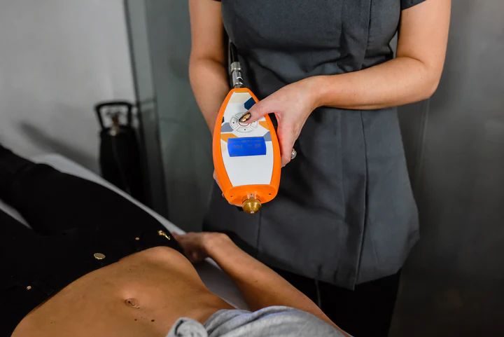 Handheld cryotherapy being applied across an adult's abdomen in a treatment room
